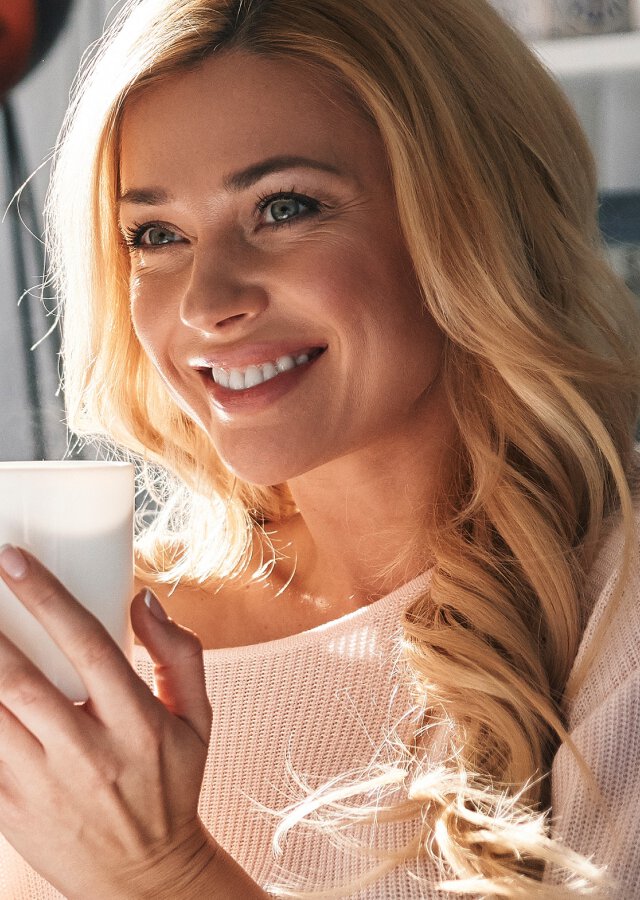Female facial plastic surgery patient, smiling and holding coffee cup